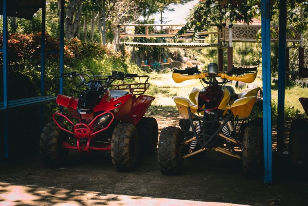 Two quad bikes parked under a shaded area surrounded by lush greenery.
