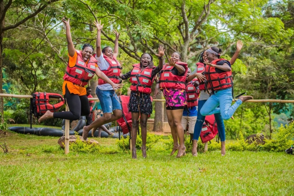 Group of women in life vests jumping joyfully in a lush Ugandan landscape.